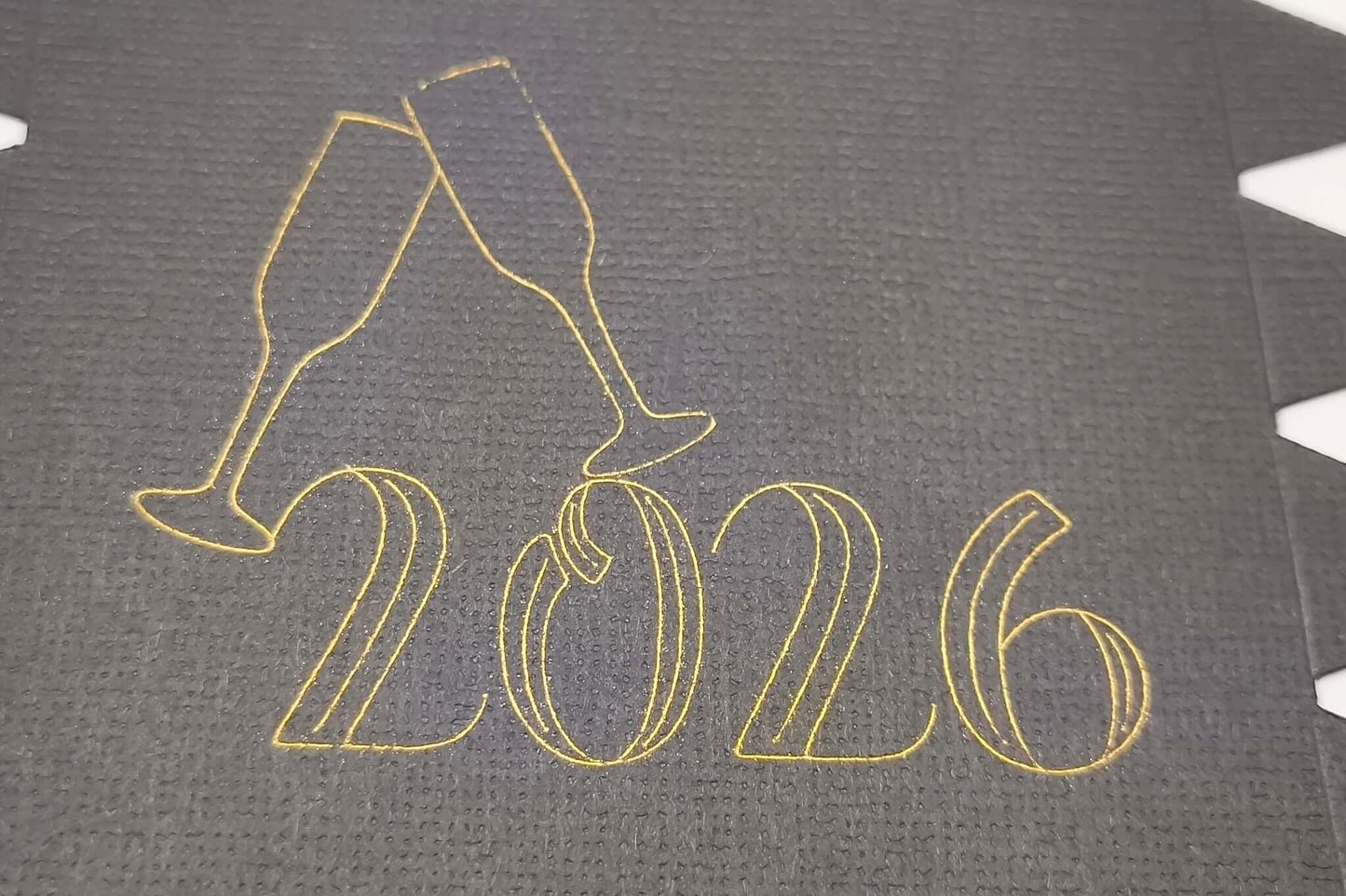 Detailed view of gold foiled “2026” with champagne glasses design on black cracker card.