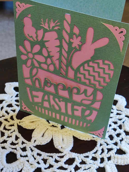 Easter greeting card featuring pink cut-out design with flowers, bunny, and eggs, celebrating springtime joy.