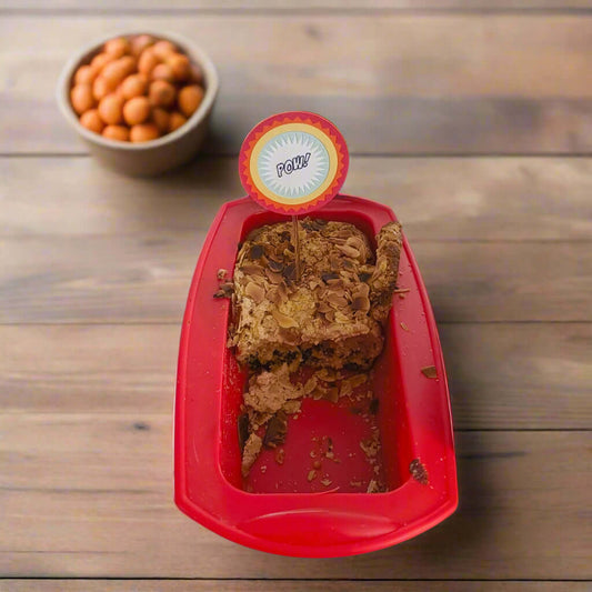 Top-down angle of superhero-style 'POW!' cake topper inserted into an almond loaf cake in a red baking tray, perfect for birthday party decor.