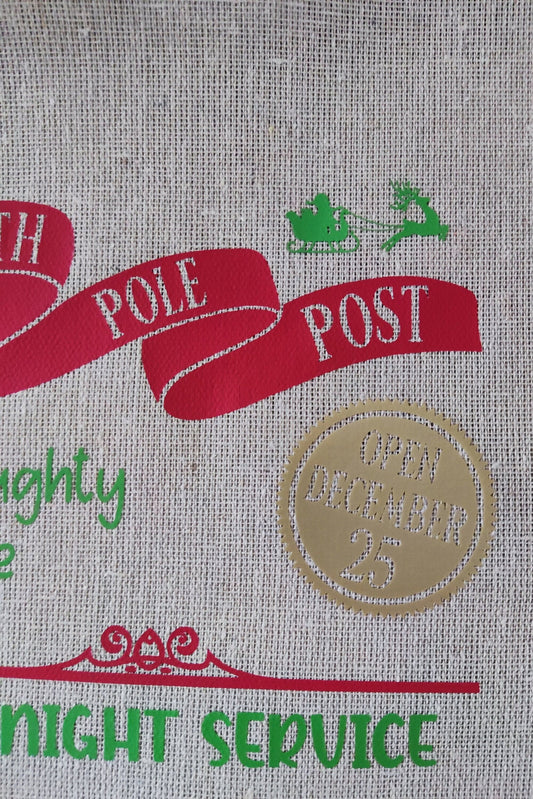 Design of a festive sack featuring 'North Pole Post' and 'Open December 25' in red and green colors.