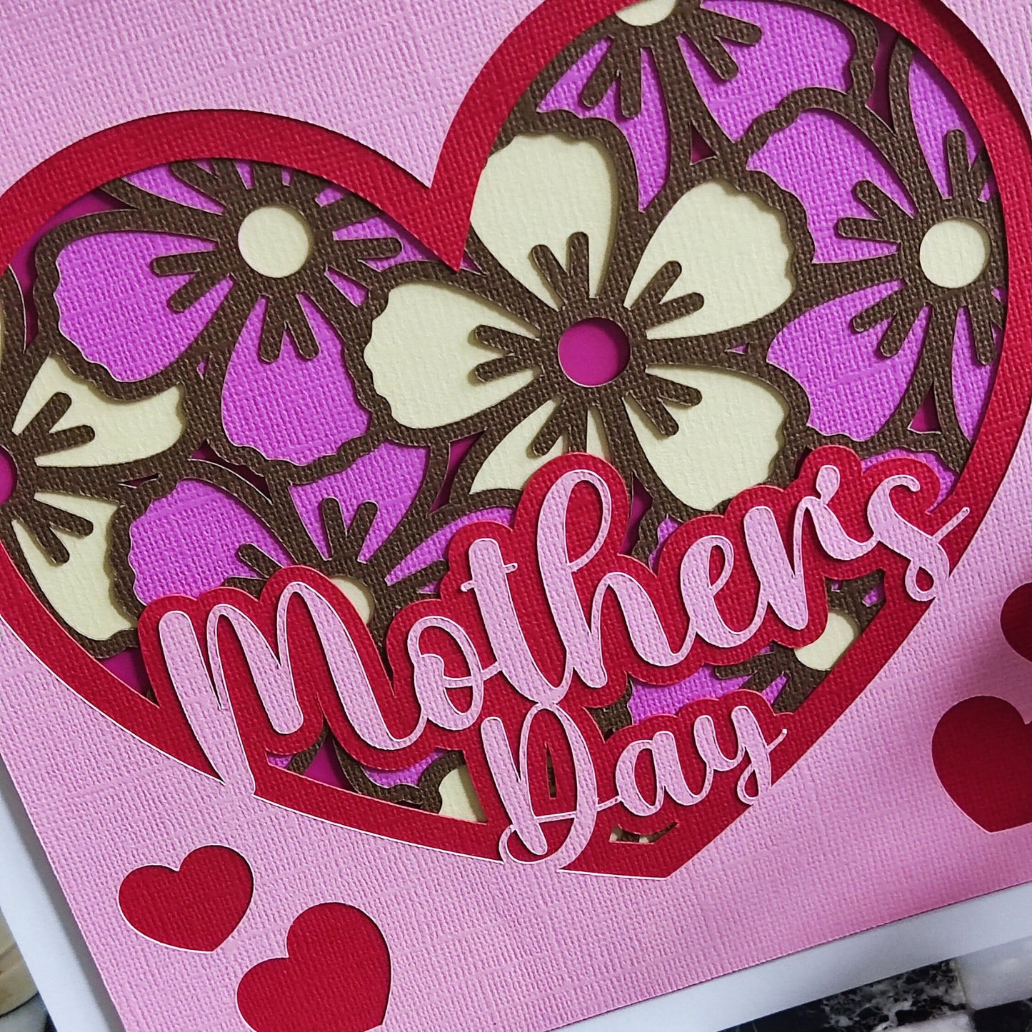 Handmade Mother's Day card with floral heart design in pink and purple, featuring cut-out flowers and layered hearts.