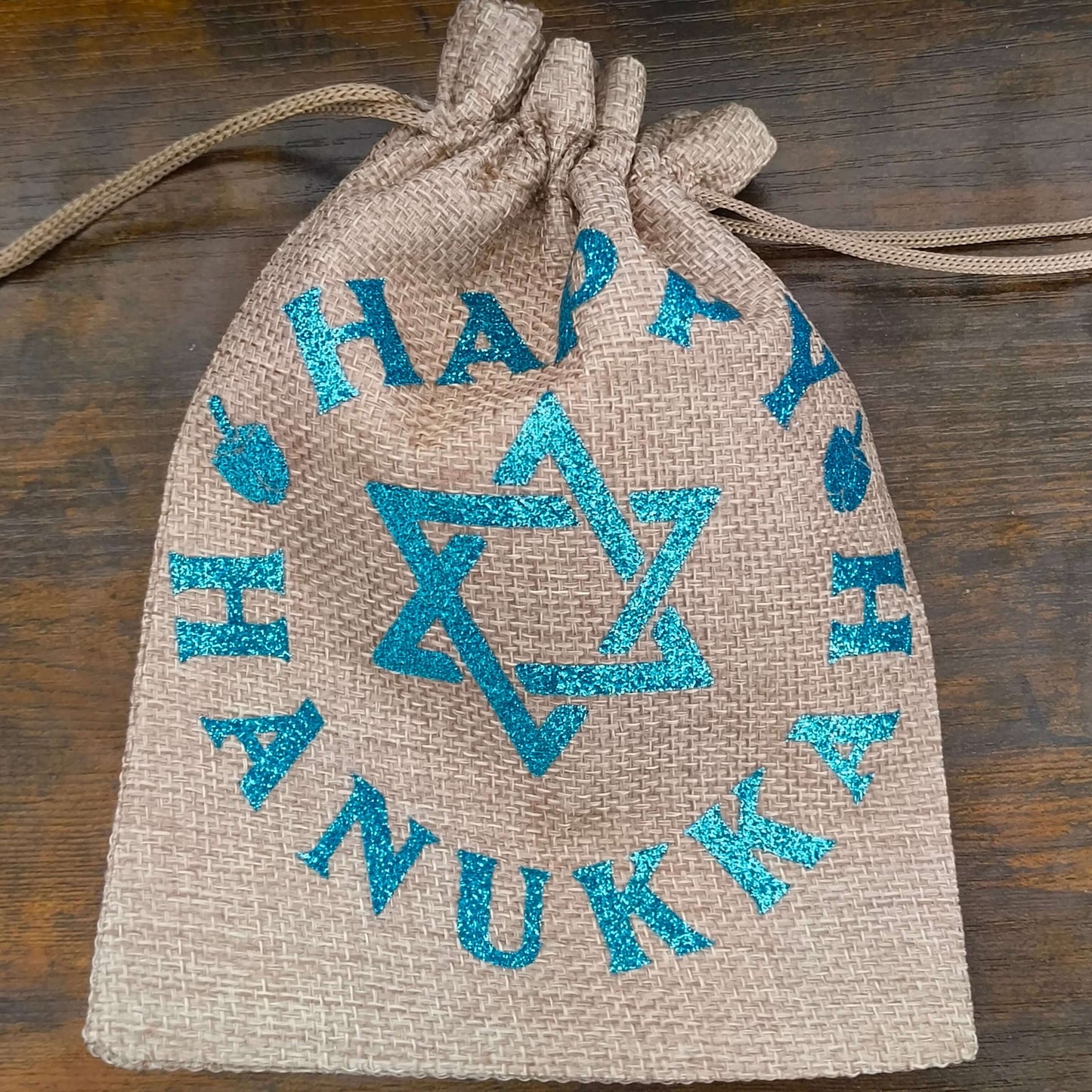 Drawstring Hanukkah hessian bag cinched at top with visible blue glitter Star of David and lettering