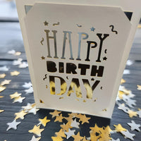 Close-up of a white laser-cut "Happy Birthday" card holder with star confetti.