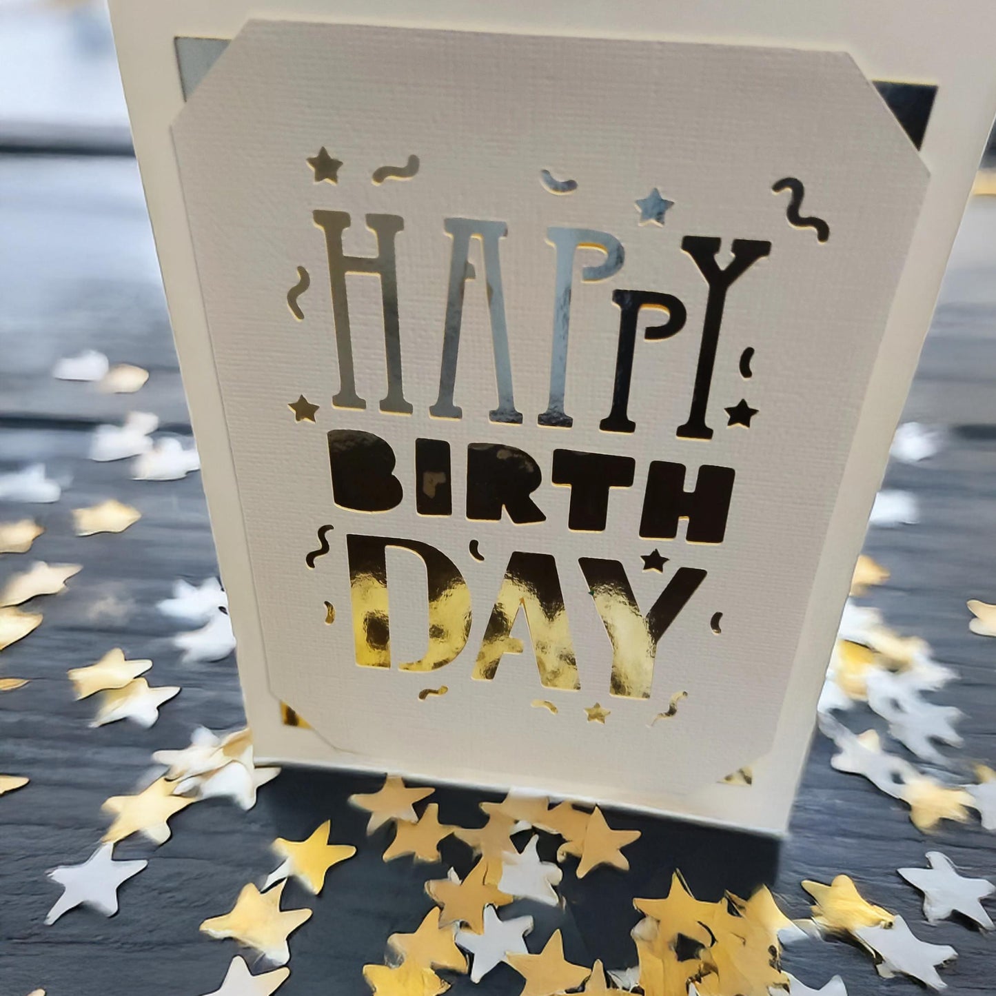 Close-up of a white laser-cut "Happy Birthday" card holder with star confetti.