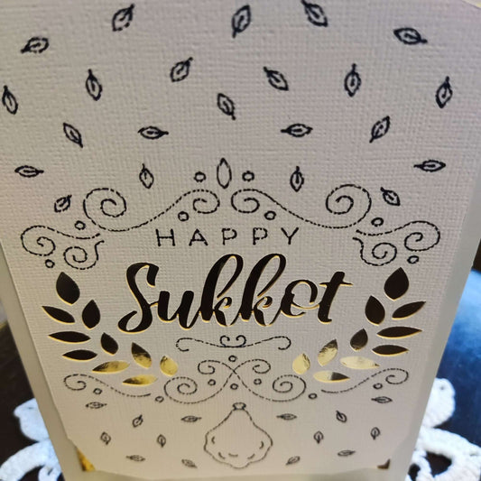 Close-up of a "Happy Sukkot" card with laser-cut text and decorative elements.