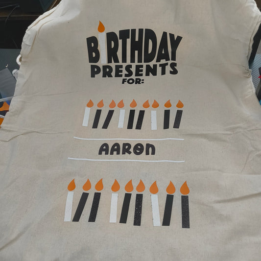 Personalised birthday gift bag with vinyl design, featuring black and white candles with orange flames and the name Aaron on a cotton sack