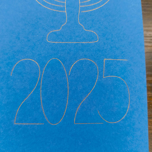 A close-up of the year '2025' finely outlined in gold on a bright blue card. The elegant, modern typography sits beneath the base of a menorah design, part of a minimalist Hanukkah-themed card.