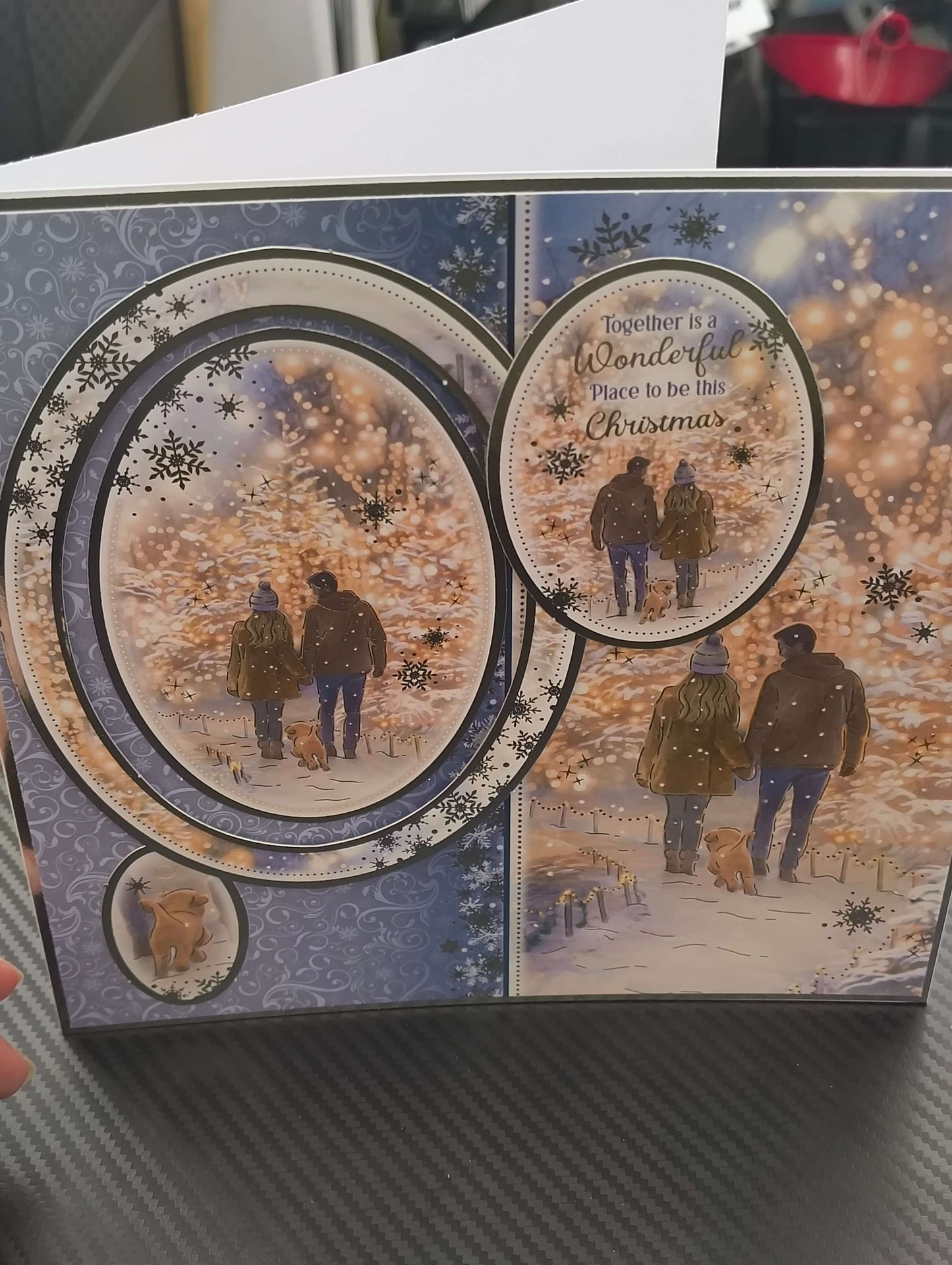 Handmade Christmas card featuring a couple walking with a dog in a snowy landscape, and festive decorations.