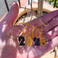Hand holding a 2026 acrylic ornament with 'Hello 2026' design, perfect for New Year celebrations.