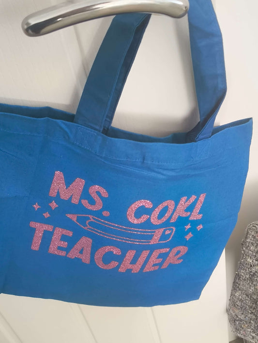 Personalised blue tote bag for teachers featuring glitter vinyl text that reads 'Ms. Gohl Teacher.' Perfect gift for educators.