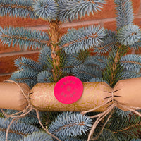 Eco-friendly Christmas crackers with gold holly design displayed on a Christmas tree branch.