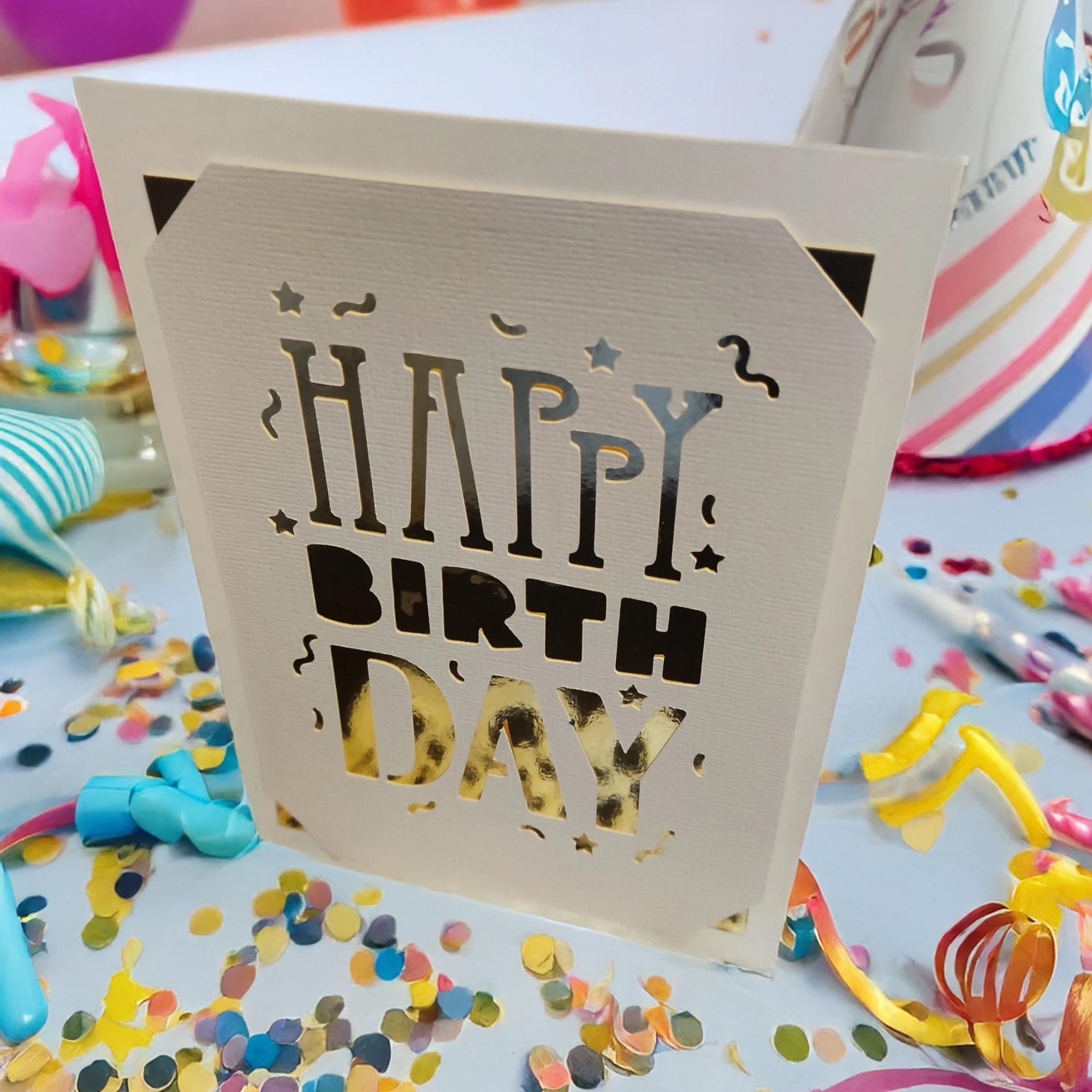 Laser-cut "Happy Birthday" card holder surrounded by festive party decorations.