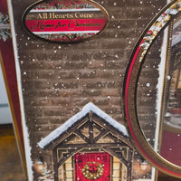 Close-up of Christmas card sentiment reading “All Hearts Come Home for Christmas” with gold edging and snowfall effect.