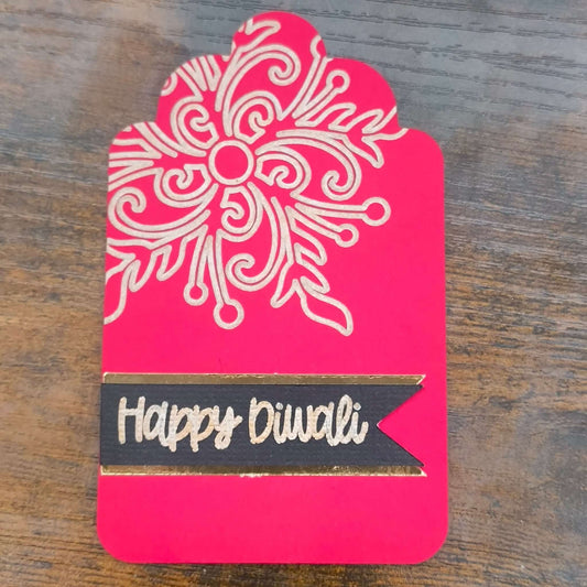 Angled side view of red Diwali tag with gold embossed floral design and black ribbon banner reading Happy Diwali