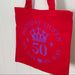 Red birthday queen tote bag with purple crown and 50th birthday design hanging neatly on door.