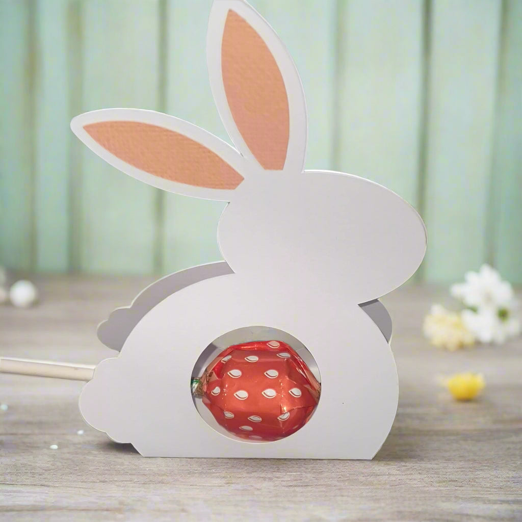 White Easter Bunny Chocolate Holder with pink ears and a red polka dot chocolate inside on wooden surface with blurred background