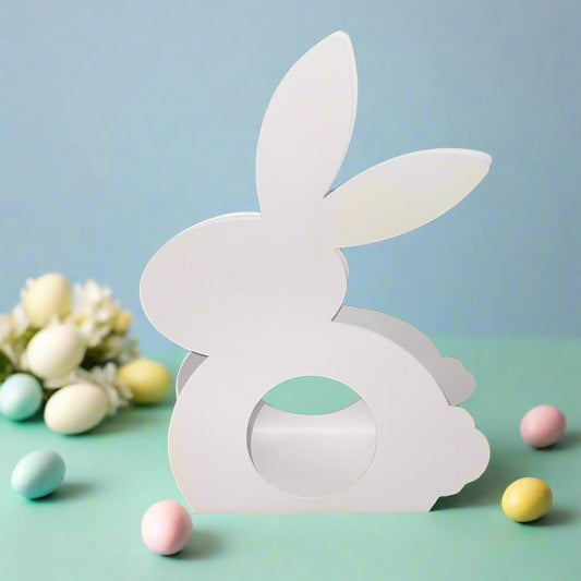 White Easter bunny-shaped chocolate holder with cutout center, surrounded by pastel Easter eggs, on a green and blue background