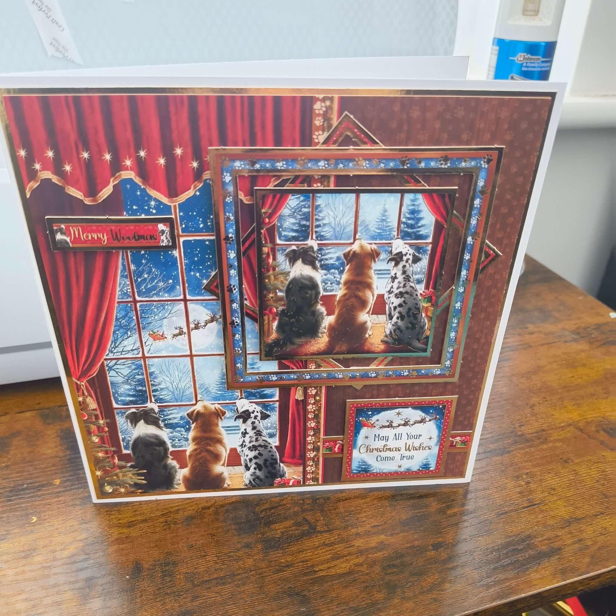 Handmade Christmas card featuring three dogs watching Santa’s sleigh through a snowy window, layered 3D design with red curtains and festive details.