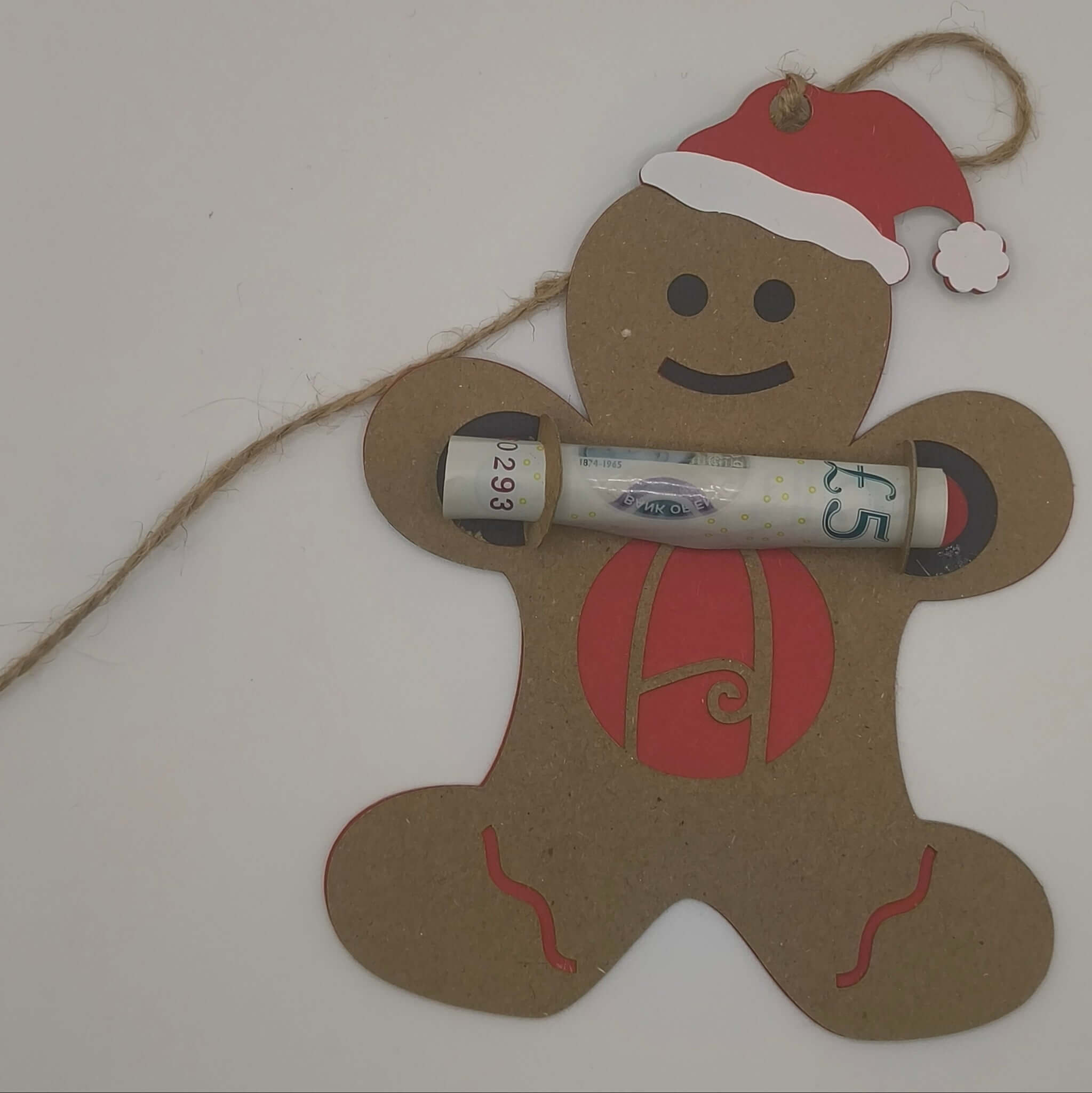 Gingerbread man ornament lying flat with rolled money gift secured in arms, showing red backing and monogram A.
