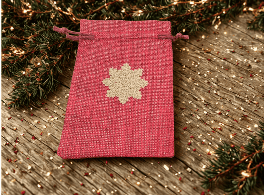 Gold snowflake gift bag in red hessian fabric on rustic wood, perfect for Christmas presents.
