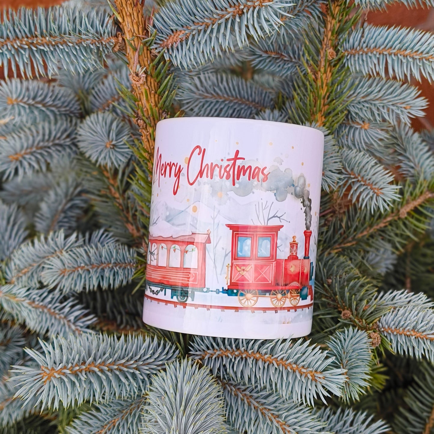 Christmas mug with festive train design hanging on blue spruce tree branch outdoors