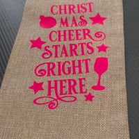 Festive hessian wine bag with pink lettering saying 'Christmas Cheer Starts Right Here', perfect for holiday gifting.