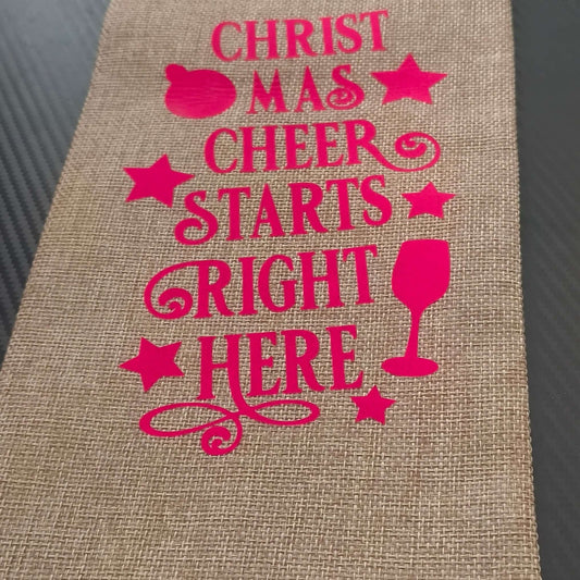 Festive hessian wine bag with pink lettering saying 'Christmas Cheer Starts Right Here', perfect for holiday gifting.