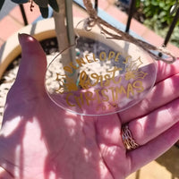 Personalised clear acrylic Christmas bauble with gold lettering reading "Penelope’s First Christmas 2025" held in hand outdoors.