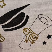 Close-up of handmade graduation card showing gold stars, diploma with ribbon, and black mortarboard on ivory textured cardstock.