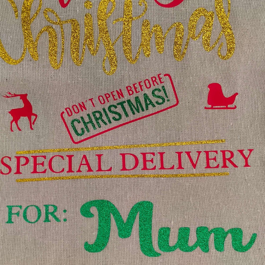 Close-up of personalised Christmas gift sack for Mum – gold glitter “Christmas” lettering, red sleigh and reindeer icons, green vinyl name detail, and festive “Don’t Open Before Christmas” stamp.