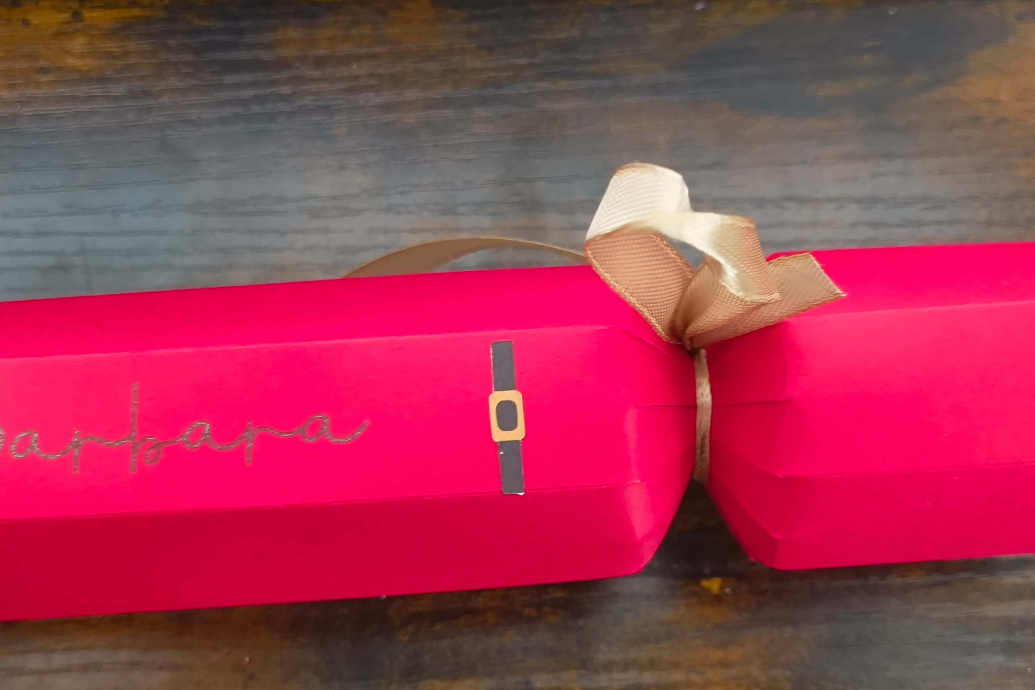 Personalised red Christmas cracker with gold ribbon and Santa design, adding festive charm to your holiday table.