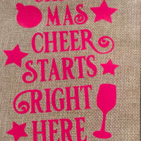 Text on hessian wine bag says 'Christmas Cheer Starts Right Here' with festive decorations.