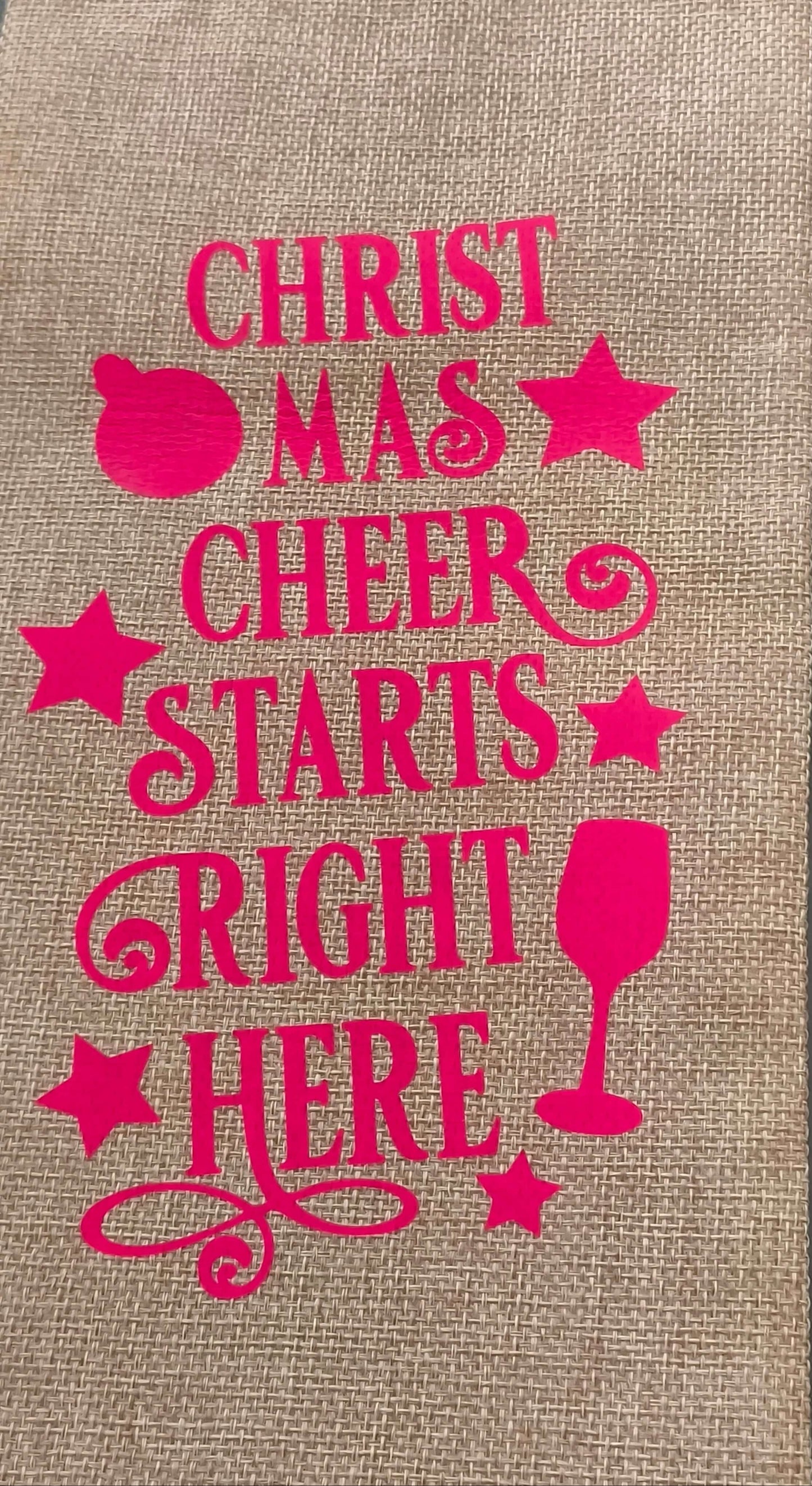 Text on hessian wine bag says 'Christmas Cheer Starts Right Here' with festive decorations.