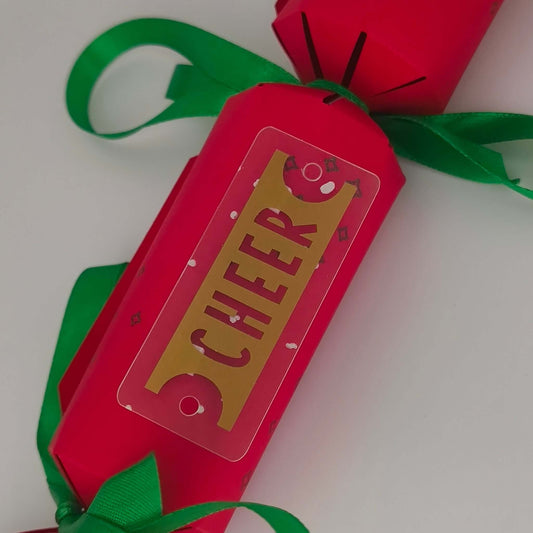 Close-up of red Christmas cracker showing gold ‘CHEER’ tag tied with green ribbon.
