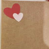 Close-up of kraft envelope with layered red and pink heart embellishments, part of handmade love card set.