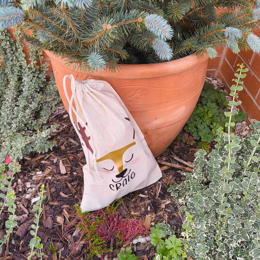Close-up of personalised fabric gift bag with golden reindeer design and name Craig, rustic outdoor setting