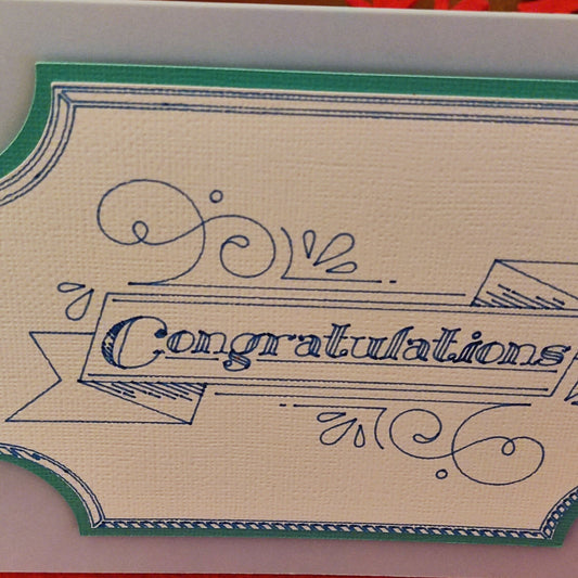 Close-up of the ornate banner design with “Congratulations” text, printed in blue on textured ivory card with a teal border. Highlights the intricate detail of the handmade finish.