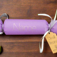 Personalised purple Diwali cracker with white ribbon and 'Diwali Blessings' gift tag, styled on a rustic wooden table with a green pear beside it.