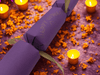 Handmade purple Diwali cracker with gold ribbon, surrounded by glowing tealight candles and marigold petals on a festive background.