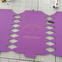 Purple card cracker template with diamond cut-outs and gold foil “Happy Diwali Festival of Lights” design, ready for folding and assembly.