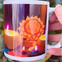 White ceramic mug featuring a vibrant Diwali design with glowing clay oil lamps (diyas) and a golden mandala pattern, held outdoors near evergreen plants.
