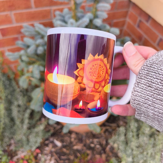 Hand holding a white Diwali-themed mug showing colourful diyas and a glowing mandala lantern design, photographed in a garden setting.