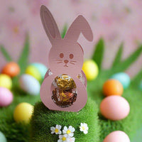 Cute Easter Bunny chocolate holder filled with Lindor chocolates, surrounded by colourful Easter eggs and grass display.
