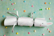 Handmade white Easter Bunny cracker with silver ribbon ties and cute vinyl bunny face on pastel background with colorful candy pieces scattered around.