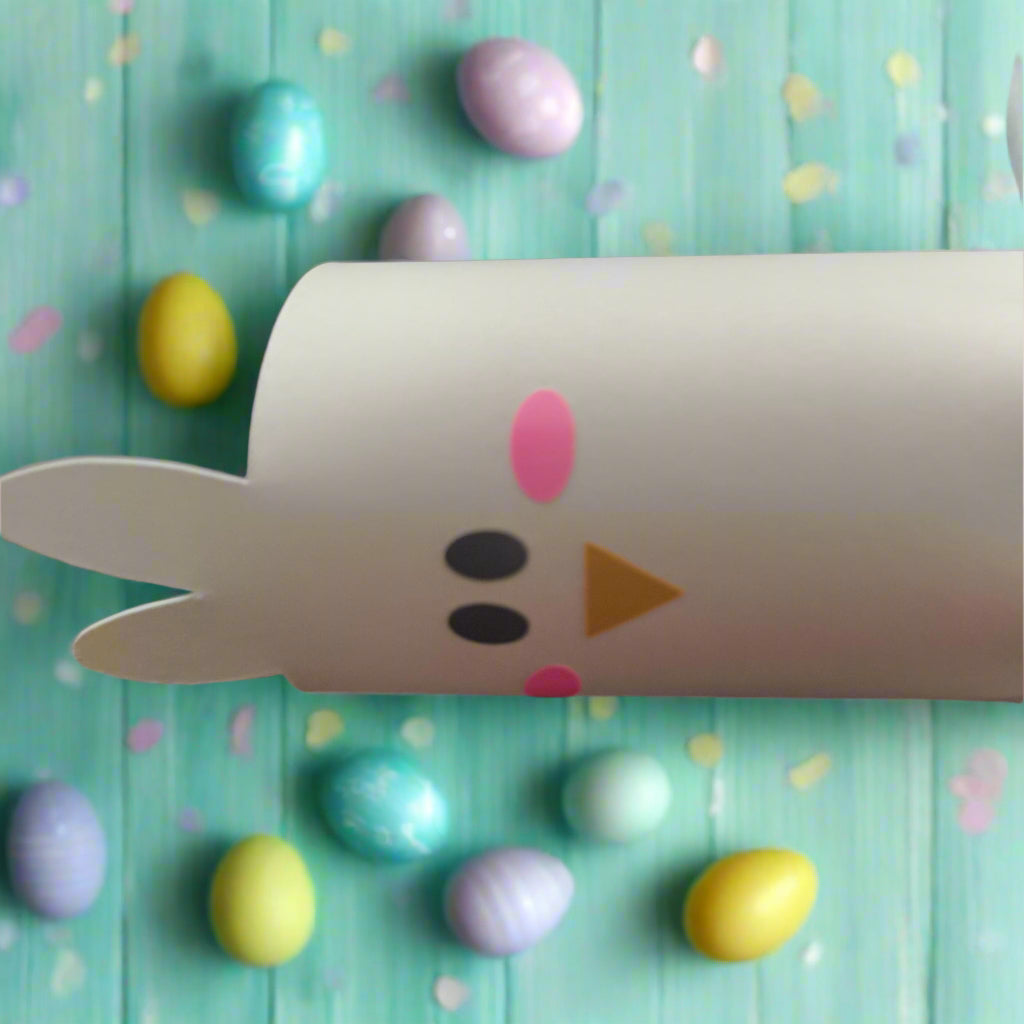Close-up of Easter cracker chick face with bunny-style ears, pink cheeks, and orange beak, surrounded by colourful painted eggs on a teal background.