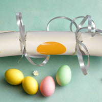 Cute chick Easter cracker in cream cardstock with pink cheeks, orange beak, and silver ribbon. Photographed with pastel eggs and small daisies.