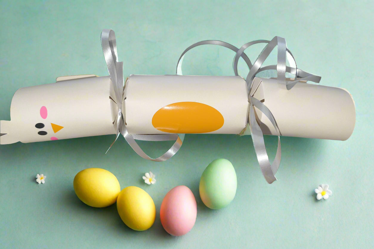 Cute chick Easter cracker in cream cardstock with pink cheeks, orange beak, and silver ribbon. Photographed with pastel eggs and small daisies.
