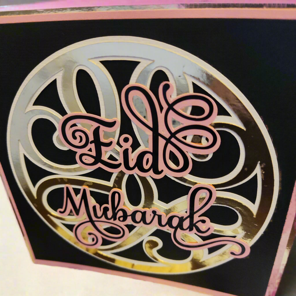 Close-up angled shot highlighting the reflective gold pattern and soft pink script, giving the card a modern yet traditional festive charm.