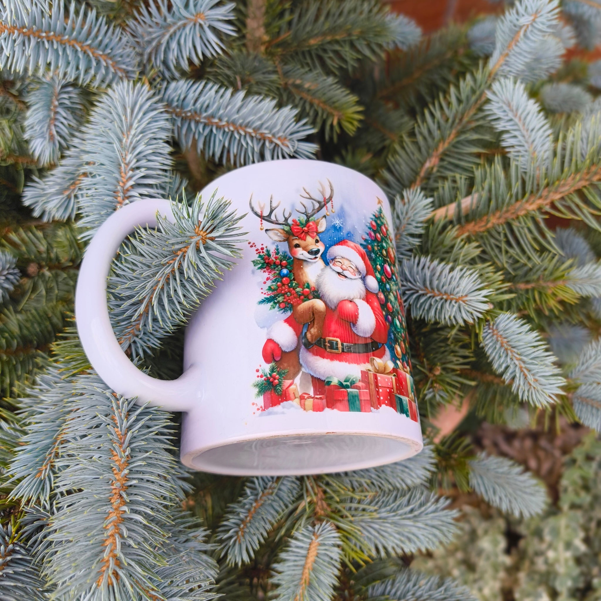Ceramic Christmas mug with Santa and reindeer, surrounded by presents and a tree, shown nestled in pine tree branches
