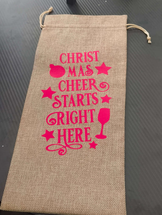 Festive hessian wine bag with pink text saying 'Christmas Cheer Starts Right Here' for eco-friendly gifting.